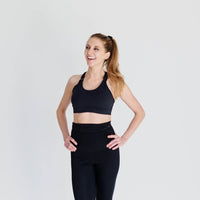 Woman showing front of strappy-back black nursing sports bra from Joyleta maternity store Canada.