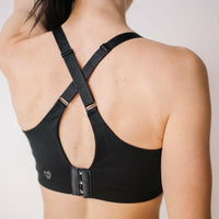 Woman showing criss cross back of black front-zip nursing sports bra.