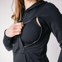 Woman wearing black maternity and nursing hoodie with hidden zippers, large hood, thumb holes and hand covers.