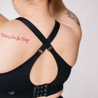 Woman showing criss cross back of black front-zip nursing sports bra.