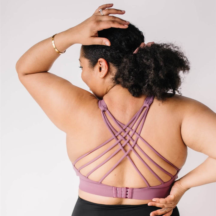 Woman wearing a strappy-back maternity and nursing sports bra in purple (wild plum) color. 