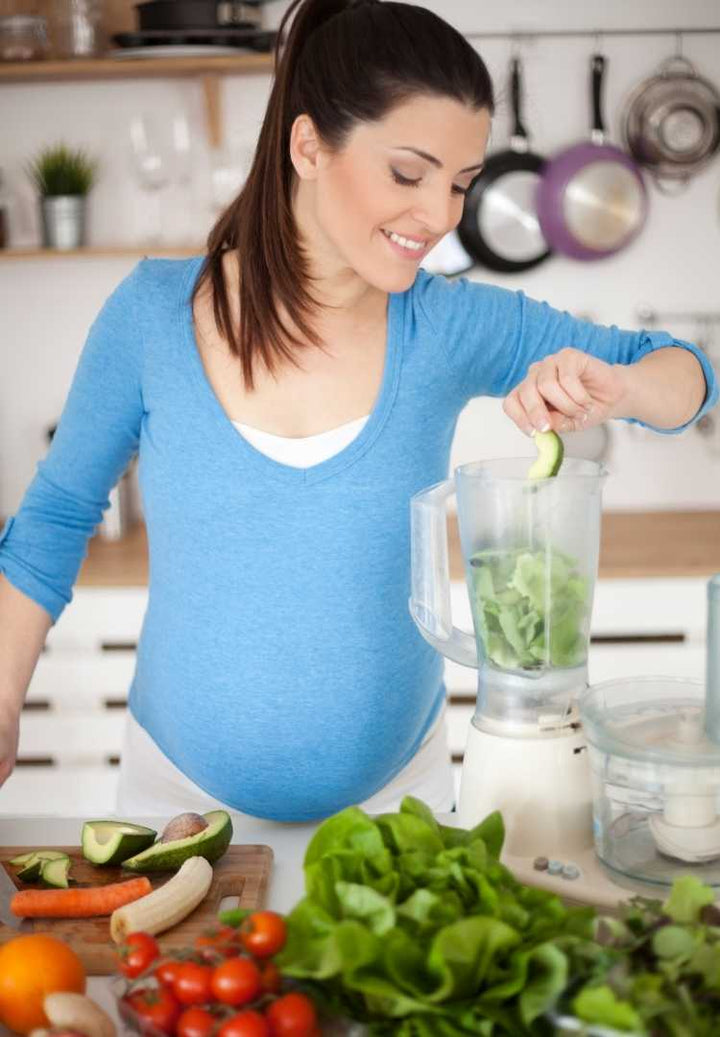 Woman holding pregnant belly beside blender of fruit for nutrition in pregnancy blog.