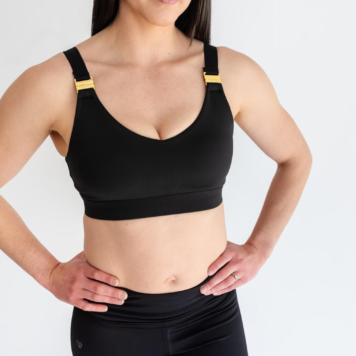 Woman showing front of black nursing sports bra with gold hardware from Joyleta maternity activewear store Canada.