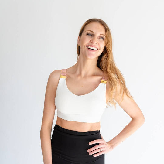 Woman showing front of white nursing sports bra with gold nursing clasps and pink straps from Joyleta, a maternity activewear store in Canada.