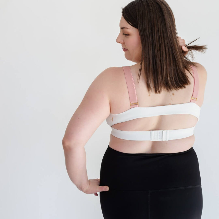 Woman showing open-back of white nursing sports bra from Joyleta maternity activewear Canada.