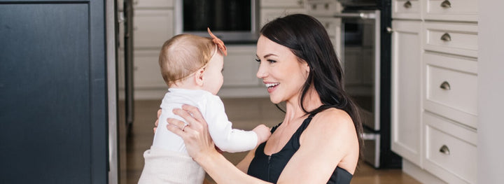 Mother wearing nursing sports bra and maternity workout leggings, holding baby and doing postnatal workout