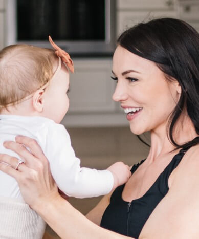 Mother wearing nursing sports bra and maternity workout leggings, holding baby and doing postnatal workout