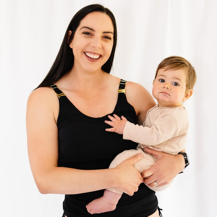 Mother holding baby and wearing black nursing swimsuit.