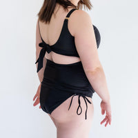 Woman showing side of black maternity swimsuit bottoms from Canadian maternity activewear company, Joyleta.