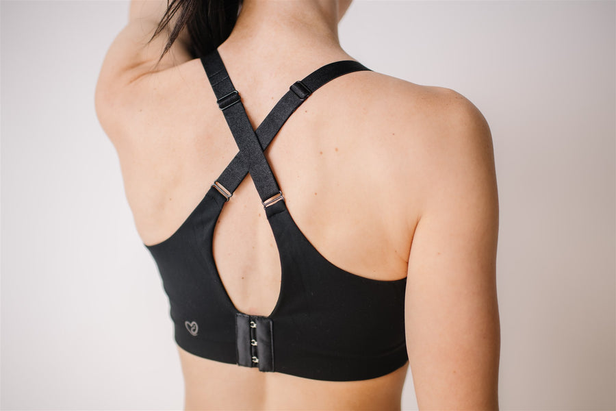 Woman showing criss cross back of black front-zip nursing sports bra.