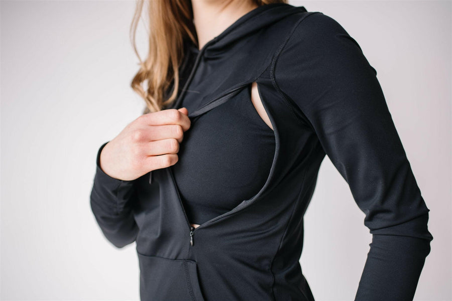 Woman wearing black maternity and nursing hoodie with hidden zippers, large hood, thumb holes and hand covers.