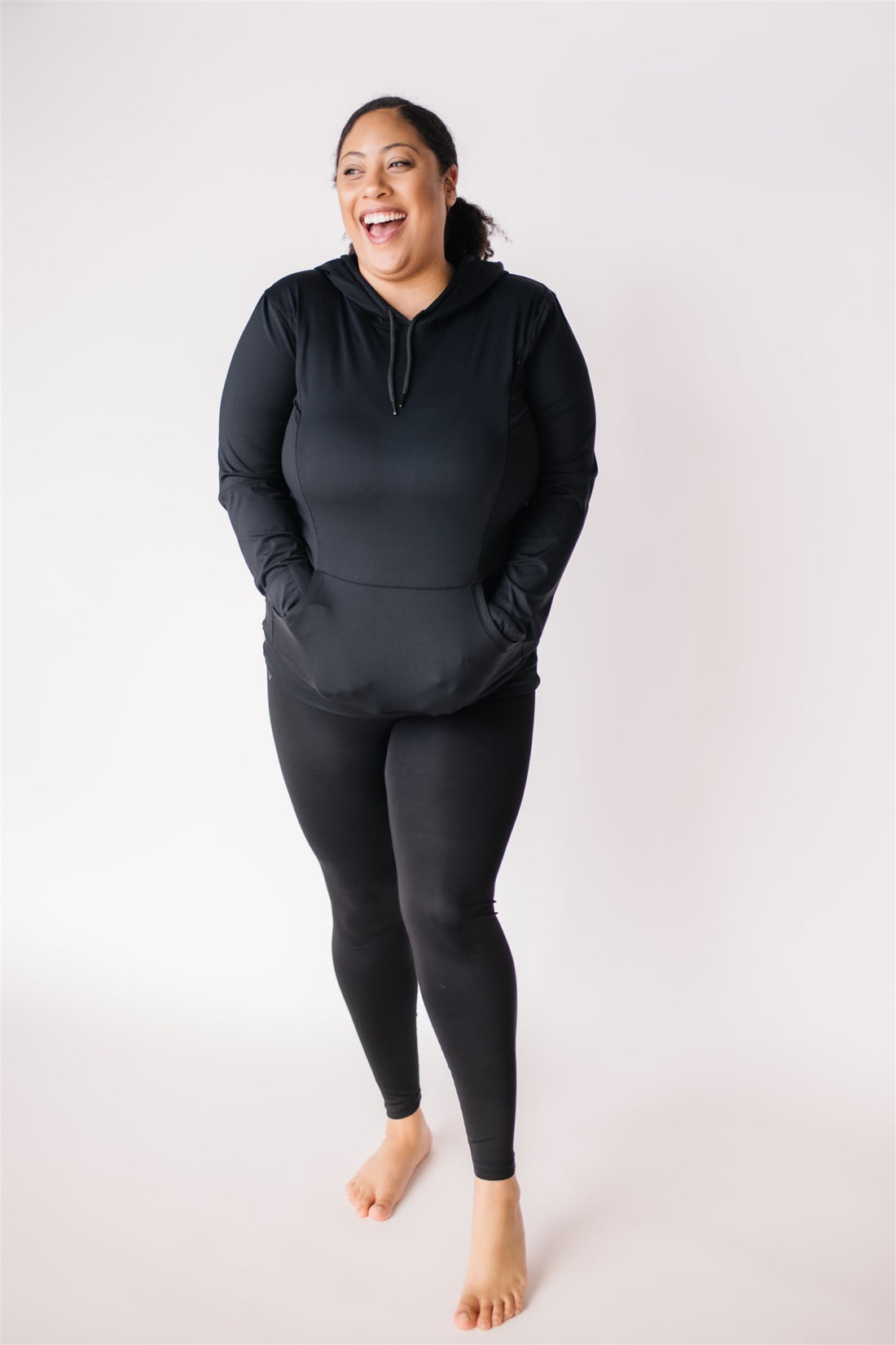 Woman wearing black maternity and nursing hoodie with hidden zippers, large hood, thumb holes and hand covers.