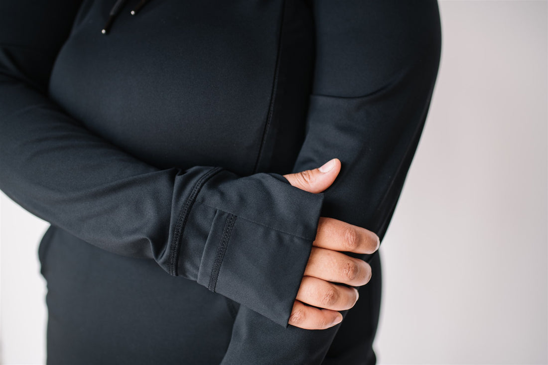 Woman wearing black maternity and nursing hoodie with hidden zippers, large hood, thumb holes and hand covers.