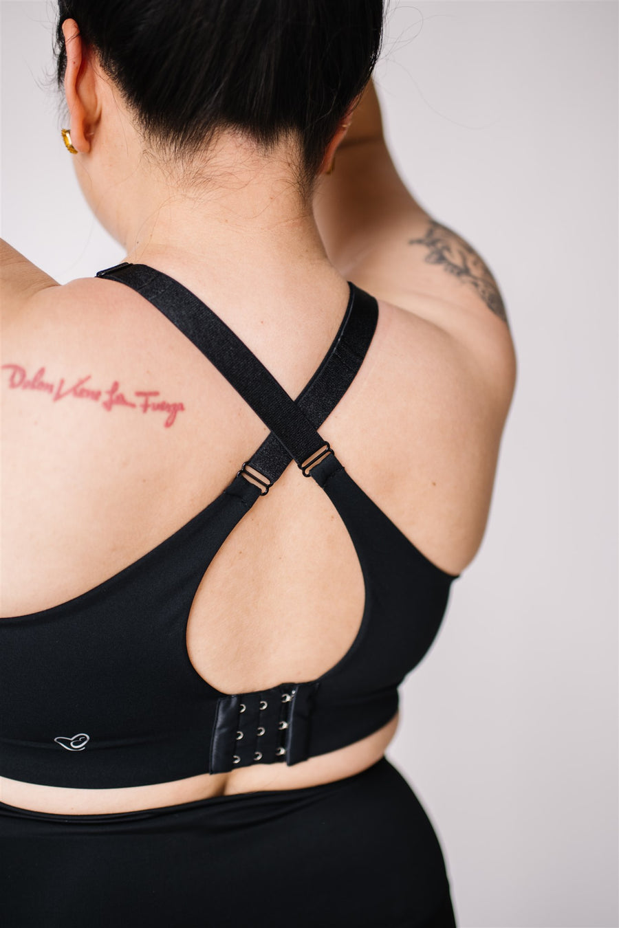 Woman showing criss cross back of black front-zip nursing sports bra.